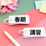 ピンクとグリーンの背景に、日本語の単語、白いペン、パステルカラーの付箋、ピンクの桜が描かれた2枚のフラッシュカード。カードには「春期」と「講習」と書かれている。.