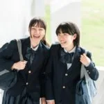 鎌倉市の明るい屋外の環境で、そろいのリボンが付いた黒い制服を着た笑顔の学生 2 人が階段に立っており、肩にランドセルを担いで、放課後の幸せそうで楽しそうに見えます。.