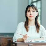 机に座って鉛筆をもっている勉強中の女子学生