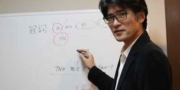 ホワイトボードに文法を教えるスーツ姿の男性。