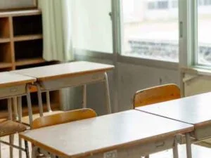 鎌倉市にある明るいEigojuku英語塾の教室には、大きな窓と棚を背景に、空いている木製の机と椅子が並べられています。差し込む陽光が、静かで落ち着いた雰囲気を醸し出しています。.