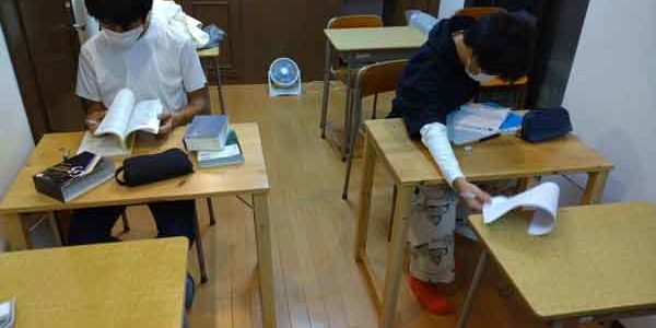 教室で勉強する二人の学生、机には教科書と文房具が並んでいます。